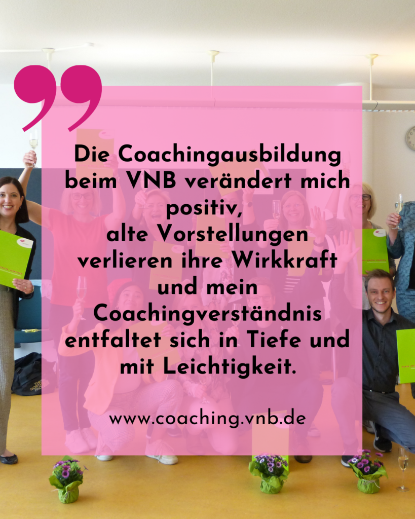 Gruppe von Menschen steht mit erhobenen Gläsern und grünen Ordnern in einem hellen Raum mit Holzboden und zwei kleinen Blumenarrangements im Vordergrund