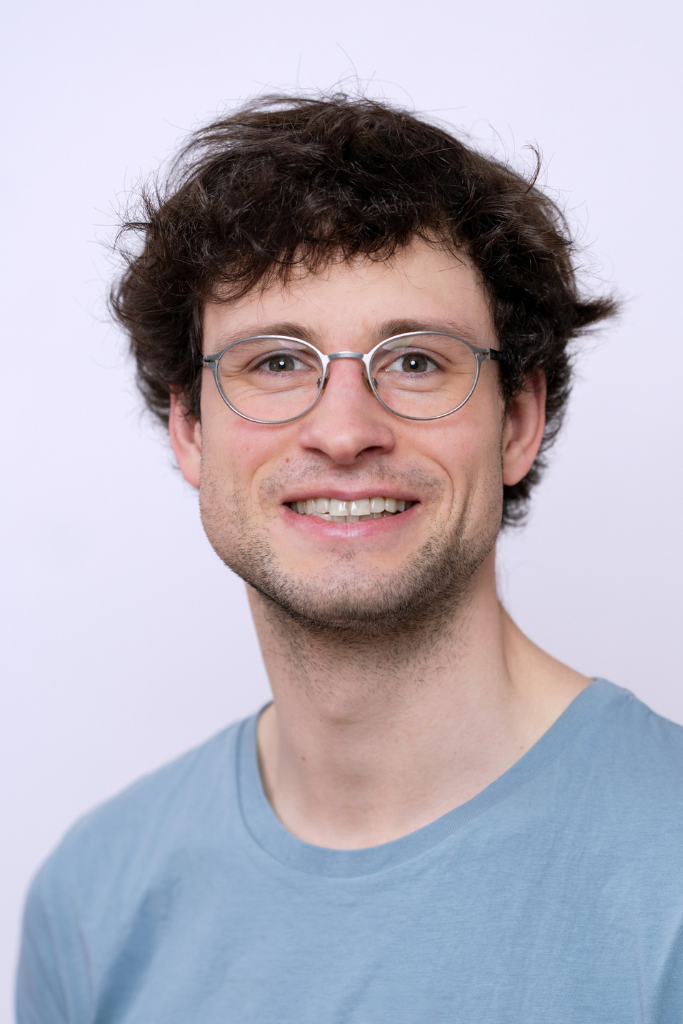 Person mit lockigen Haaren und hellblauem T-Shirt vor hellem Hintergrund