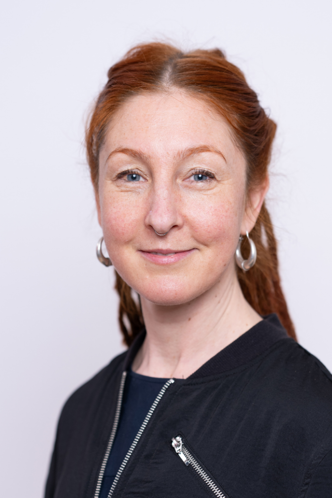 Frau mit dunkler Jacke und silbernen Creolen vor hellem Hintergrund