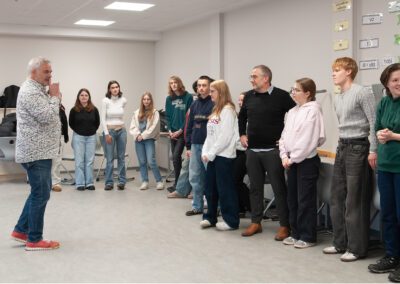 Gruppe von Menschen steht in einem Halbkreis in einem hellen Raum, eine Person spricht vor der Gruppe