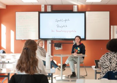 Jugendliche sitzen in einem Klassenraum vor einem Bildschirm mit der Aufschrift 'Spotlight Projekt Das Bewerbungsgespräch'