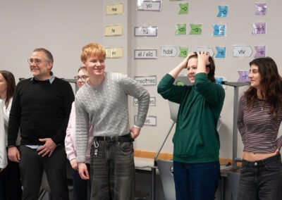 Gruppe von Jugendlichen steht vor einer Wand mit farbigen Wortkarten in Spanisch und macht gestische Übungen